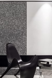 Minimalist black chair against a speckled terrazzo wall and a white wall, illuminated by ambient lighting.