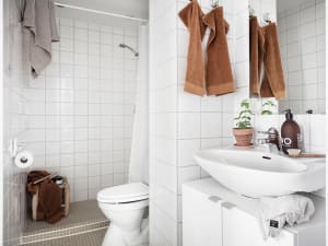 A minimalist bathroom with white ceramic tiles, a white toilet, a white sink, and brown towels hanging on the wall.