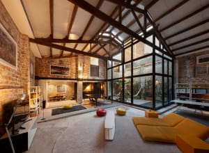 A spacious modern living room with exposed brick walls and large windows, featuring contemporary furniture and minimalist des
