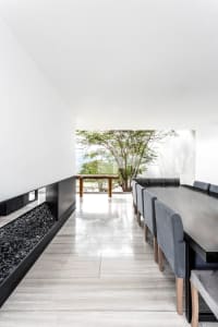 A modern minimalist dining room featuring concrete flooring and walls, with a long dining table, grey upholstered chairs, and
