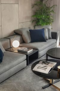 A modern living room with a gray fabric couch, black round side tables with glass tops, and a potted plant in the corner.