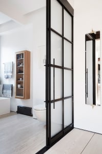 A modern bathroom with white furniture and a frosted glass door.