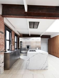 A modern residential kitchen featuring metal appliances, brick walls, and a marble island.