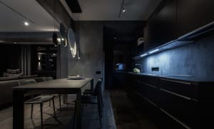 A modern residential kitchen with concrete walls and a black dining table with chairs.