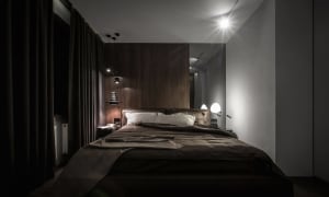 A modern bedroom featuring a wooden panel wall, a queen-sized bed with a dark comforter, and two bedside lamps.
