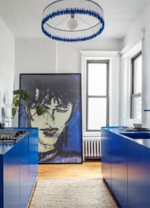 A modern kitchen with blue cabinets and a large window allowing natural light to flood the space. The ceiling features a uniq