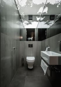 A modern bathroom with concrete walls, a white toilet, and a white sink with a chrome faucet.