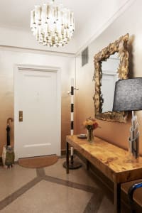 A modern entryway featuring a wooden bench, metal lamp, and vase of flowers.
