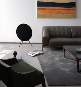 Modern minimalist living room featuring a brown leather sofa with wooden legs, a green upholstered chair, a black round speak