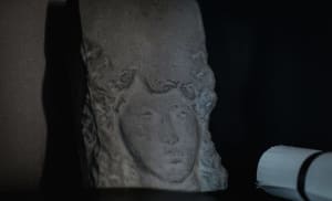 Detail of an ancient stone sculpture profile with a dark background and a light source on the right side.