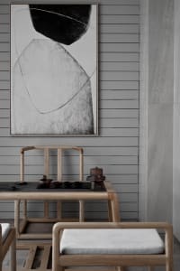 Minimalist tea room featuring wooden furniture, stone pavement, and a black and white abstract painting on the wall.
