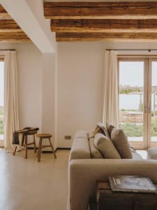 A minimalist living room featuring wooden beams, concrete floors, and upholstered furniture with fabric cushions.