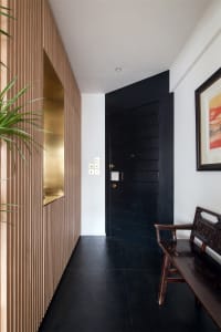 A modern entryway featuring black wooden walls and flooring, with a black door and wooden bench.