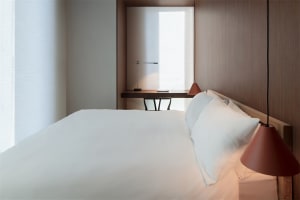 A modern minimalist bedroom with a large bed, wooden headboard, and red pendant lights.