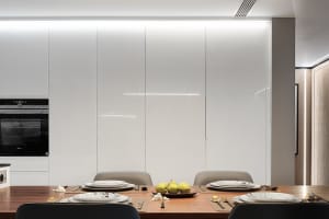 A modern kitchen with white glass tiles on the walls and wooden floor.
