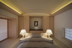 A modern minimalist bedroom featuring a bed with a light gray duvet, two table lamps on nightstands, wooden walls and floors,