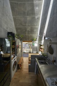 Modern minimalist kitchen with a concrete ceiling and floor, featuring a sink, stove, and washing machine
