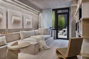 Modern living room with concrete walls, white furniture, and a view of an outdoor patio.