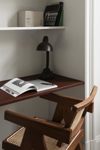 A minimalist home office featuring wooden furniture and a bookshelf with books and a lamp.