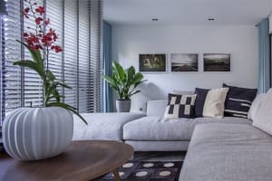 Modern minimalist living room with grey L-shaped sectional sofa, patterned cushions, wooden coffee table, floor-to-ceiling wi