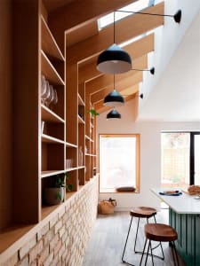 A cozy, modern residential kitchen with wooden shelves, black pendant lights, and a green kitchen island.