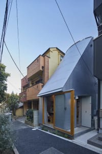 A modern residential exterior with a metallic cladding design, featuring large windows and a curved roof.