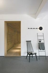 A minimalist residential interior featuring a black chair, a ladder, a bookshelf, and a book on the chair.