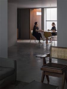 Two women sitting at a dining table in a minimalist interior with a concrete floor.