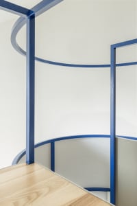 Modern interior design featuring a blue railing with curved sections and wooden flooring.