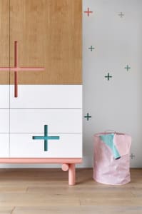 A modern wooden cabinet with pink and turquoise cross handles and a pink fabric storage basket nearby.