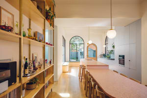 A modern kitchen featuring a pink terrazzo countertop and stools next to a wooden table and bookshelves.