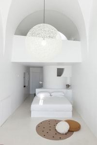 Minimalist bedroom with white bed, round light fixture, and fabric accents.