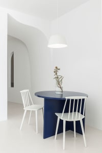 A modern minimalist dining room features a blue table with white chairs.
