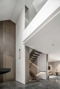 A modern interior featuring a staircase intersection with concrete flooring, minimalist lighting, and wood and glass material
