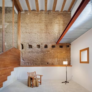 minimalist-style living room with exposed concrete walls and simple wooden furniture, including a chair with a woven backrest