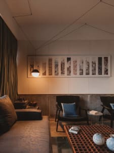 A cozy modern living room with concrete walls, textured furniture, and a large artwork.