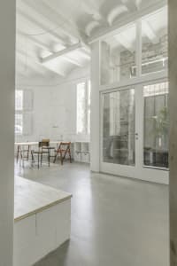 Modern minimalist office space with concrete walls, glass door, and wooden furniture.