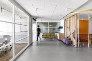 A modern office lounge with glass panels, a concrete floor, and minimalistic design elements.