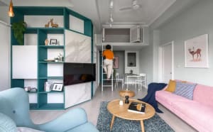 An image of a modern living room featuring a pink sofa, a blue armchair, and a green bookshelf.