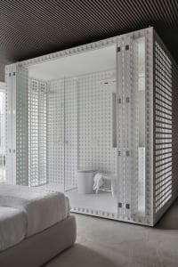 A modern bathroom with a white plaster shower enclosure and a white bed in the foreground.