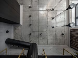 A modern industrial interior design featuring a concrete wall with exposed wiring and black cylindrical elements.
