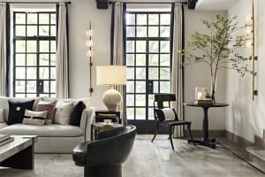 A modern minimalist living room with neutral tones and clean lines, featuring a gray couch, black chairs, and a dark wood cof
