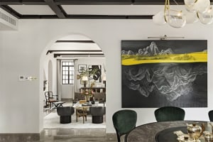 A modern dining room with a round marble table, green velvet chairs, and a large abstract art piece featuring yellow and blac