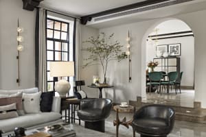 Modern living room with marble and glass decor, featuring a grey sofa, black chairs, and a glass table.