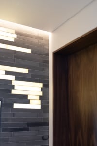 A modern interior space featuring a tiled wall with illuminated horizontal strips of lighting.