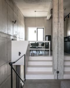 A modern, minimalist living space with concrete walls and floors, featuring a staircase leading to an upper level.