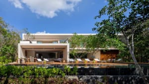 Modern residential house featuring concrete and glass exterior with a pool and lush greenery in the foreground.