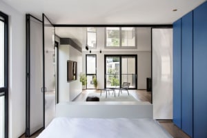 Modern minimalist bedroom with white walls, glass walls, and wood flooring.