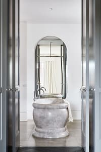 A modern bathroom with a marble bathtub and a tall, oval-shaped mirror on the wall.