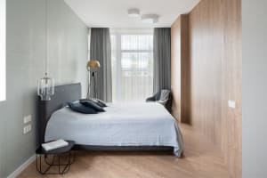 Modern bedroom featuring a grey upholstered bed with navy blue pillows, a bedside table with a lamp, and wooden paneling on o